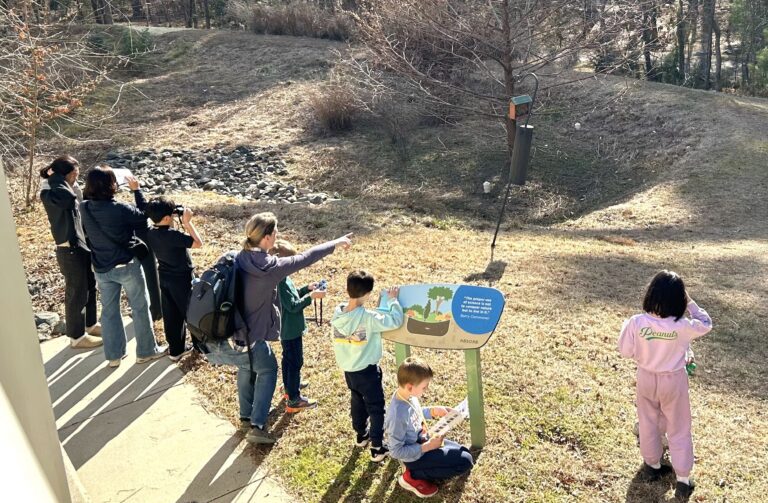 Group of kids at educational birdwatching event, with binoculars and a bird feeder