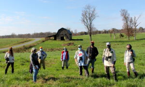 Group of people standing in a field with a barn in the background
